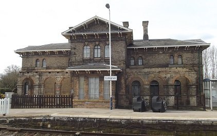 Station House Collingham, brown stone building with round arched windows in front of a platform