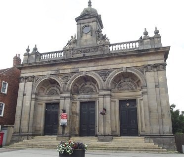 white building with three large arched doorways, sone railings and monument above 