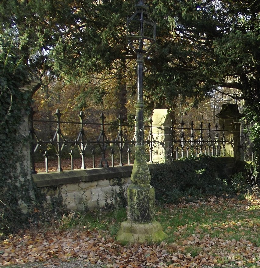 black lamp on stone base in front of iron railings, between trees