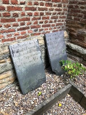 two dark headstones leaning against red brick wall