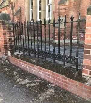 black iron railings in red brick wall with brick building behind