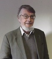 a white man with grey hair and beard in a brown suit