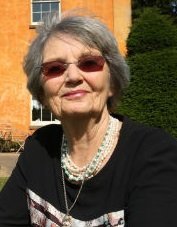a photo of a woman with short grey hair and sunglasses in a black top and a pear necklace