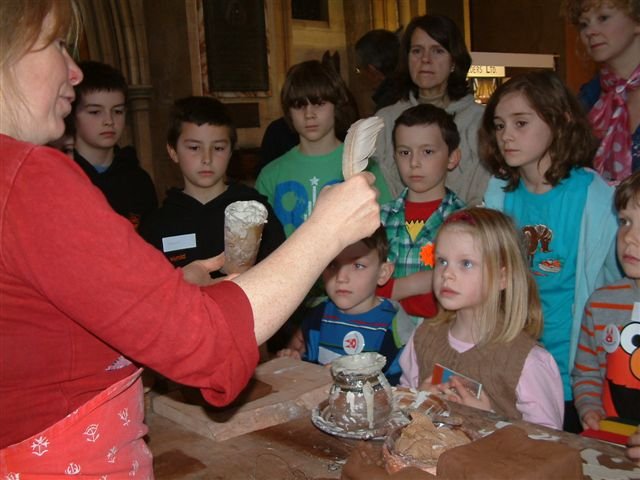 A woman making a tile in front of a group of children