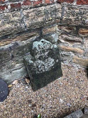 headstone leaning against stone wall
