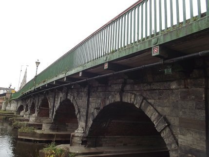 stone arched bridge with multiple arches, green railings above